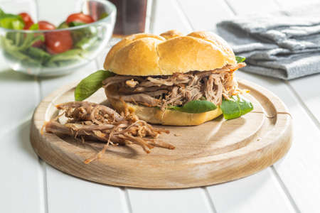 Sandwich with pulled meat on cutting board.