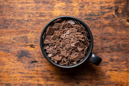 Grated dark chocolate. Chocolate flakes in cup on wooden table. Top view.