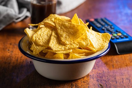 Salted tortilla chips. Yellow nachos triangle and tv remote control on wooden table.の写真素材