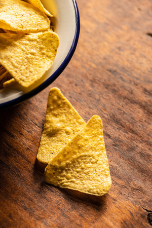 Salted tortilla chips. Yellow nachos triangle on wooden table.