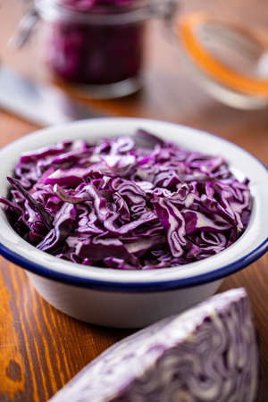 Sliced fresh red cabbage in bowl on wooden table.