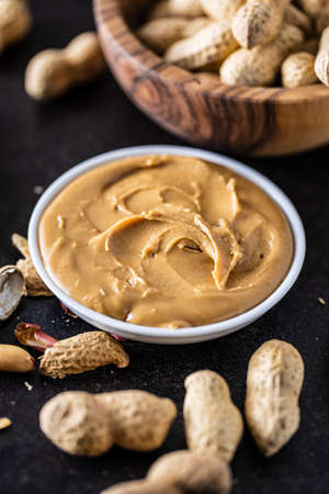 Peanut butter in bowl and peanuts on black table.