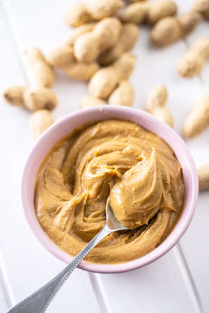 Peanut butter in bowl and peanuts on white table.
