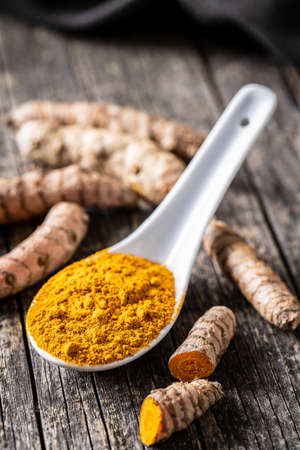 Indian turmeric powder and root. Turmeric spice. Ground turmeric in ceramic spoon on wooden table.の写真素材