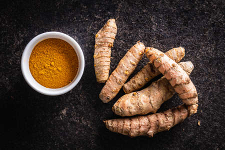 Indian turmeric powder and root. Turmeric spice. Ground turmeric in bowl on black table. Top view.の写真素材