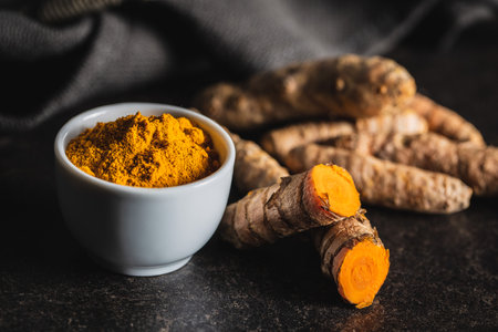 Indian turmeric powder and root. Turmeric spice. Ground turmeric in bowl on black table.の写真素材