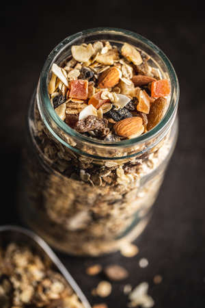 Beakfast cereals in jar. Healthy muesli with oat flakes, nuts and raisins on black table.の写真素材
