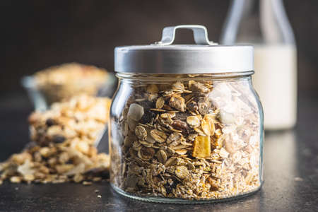 Beakfast cereals in jar. Healthy muesli with oat flakes, nuts and raisins on black table.の写真素材