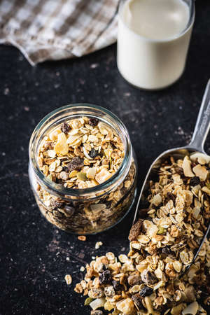 Beakfast cereals in jar. Healthy muesli with oat flakes, nuts and raisins on black table.