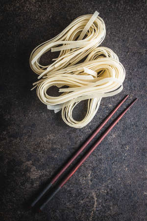 Dried white rice noodles. Raw pasta. Uncooked noodles on black table. Top view.の写真素材