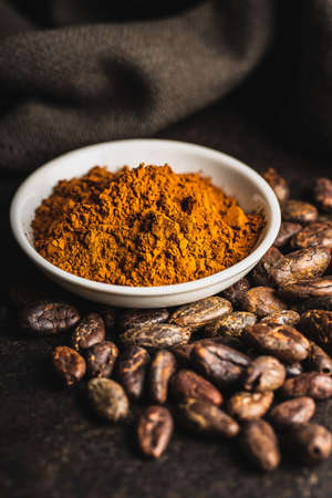 Cocoa powder and cocoa beans in bowl on black table.