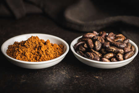 Cocoa powder and cocoa beans in bowl on black table.