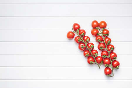 Fresh red cherry tomatoes. Small tomatoes on a branch on a white table. Top view.の写真素材