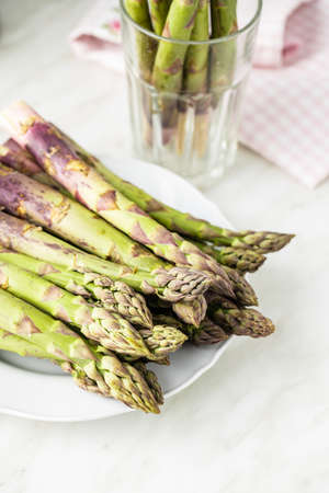 Fresh raw uncooked green asparagus on plate on white table.の写真素材