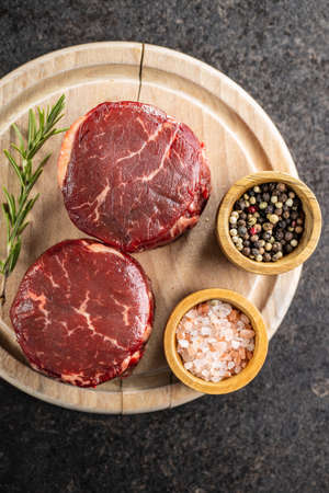 The raw beef meat steak with salt, pepper and rosemary on cutting board. Top view.の写真素材