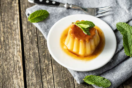 Sweet vanilla pudding. Sweet dessert with caramel topping on wooden table.の写真素材