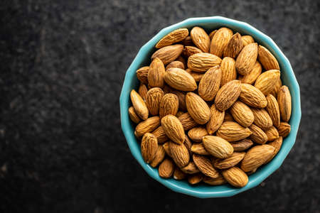 Almond nuts in bowl on a black table.