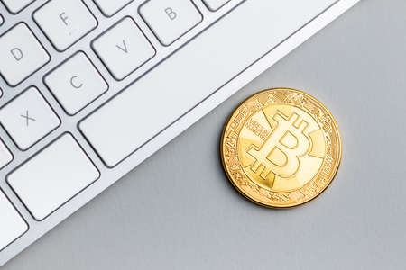 Golden bitcoin coin. Cryptocurrency and computer keyboard on gray background. Top view.