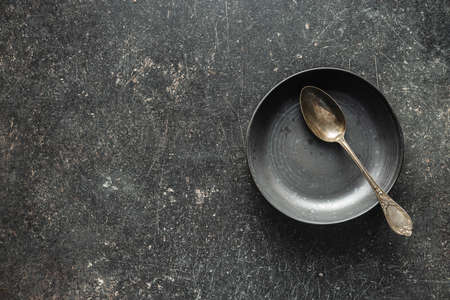 Empty vintage plate with silver spoon on black table. Top view.