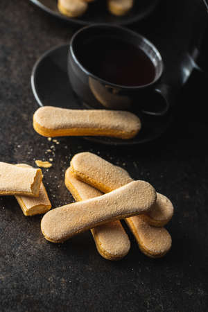 Italian cookie savoiardi. Sweet biscuits. Sponge cookies tiramisu on black table.