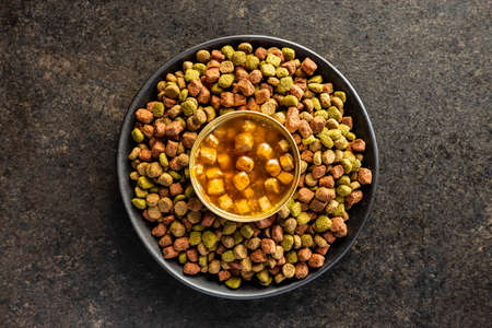 Canned pet food and dried kibble on plate. Tasty food for dog or cat on black table. Top view.