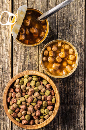 Canned pet food and dried kibble. Tasty food for dog or cat on wooden table. Top view.