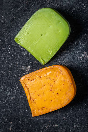 Block of hard cheese with chili and wasabi flavor on black table. Top view.の写真素材