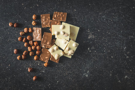 Nutty white and dark chocolate with hazelnuts on black table. Top view.