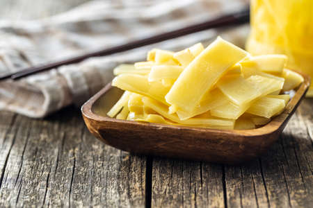 Sliced canned bamboo shoots in wooden bowl on wooden table.
