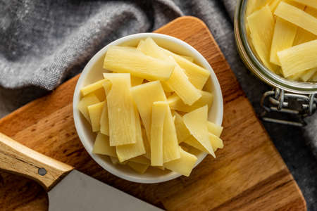 Sliced canned bamboo shoots in bowl on cutting board. Top view.