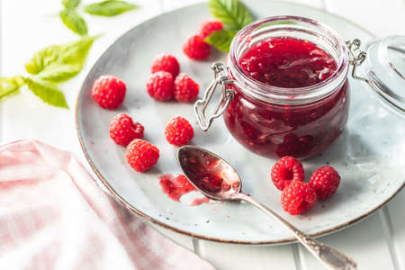 Red rasberries jam in jar and ripe raspberries on plate.の写真素材