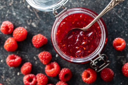 Red rasberries jam in jar and ripe raspberries on black table. Top view.の写真素材