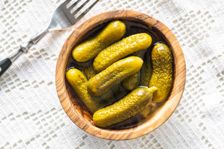 Small pickles. Marinated pickled cucumbers in wooden bowl on white table. Top view.の写真素材
