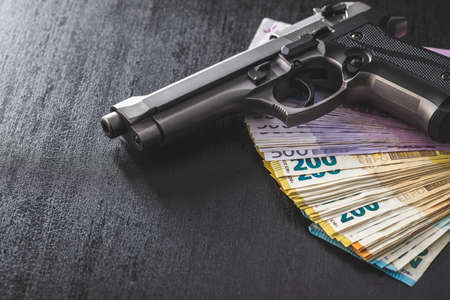 Hand gun and euro banknotes on black table.の写真素材