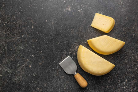 Block of hard cheese on black table. Top view.