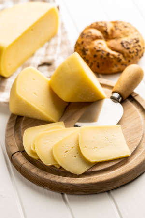 Block of hard cheese. Sliced cheese on cutting board.
