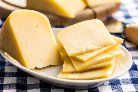 Block of hard cheese. Sliced cheese on plate.