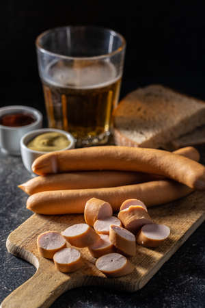 Sliced smoked frankfurter sausages on cutting board on black table.の写真素材
