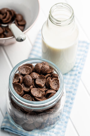 Sweet chocolate breakfast cereal flakes in jar on white table.