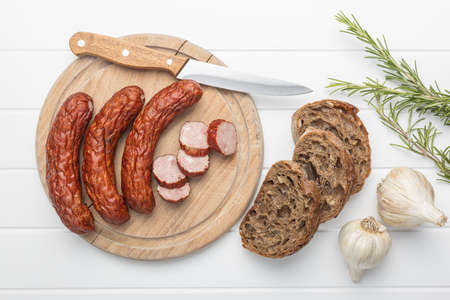 Smoked pork sausages on cutting board. Sliced salami on white table. Top view.
