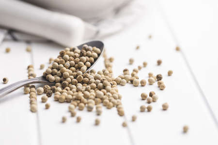 Whole pepper spice. White peppercorn grain on spoon on white table.