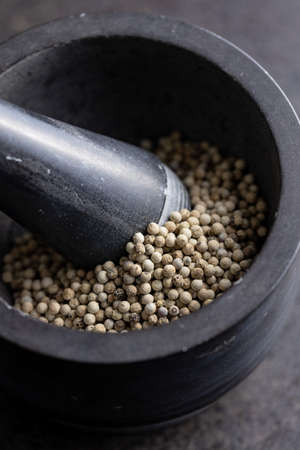 Whole pepper spice. White peppercorn grain in mortar on black table.