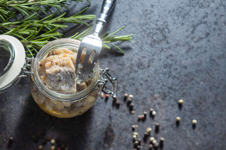 Chopped marinated fish. Salted herring in jar on black table.
