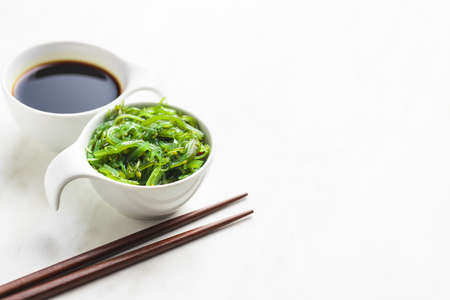 Green wakame. Seaweed salad and soy sauce in bowl on white table.