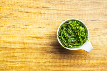 Green wakame. Seaweed salad in bowl on a wooden table. Top view.の写真素材