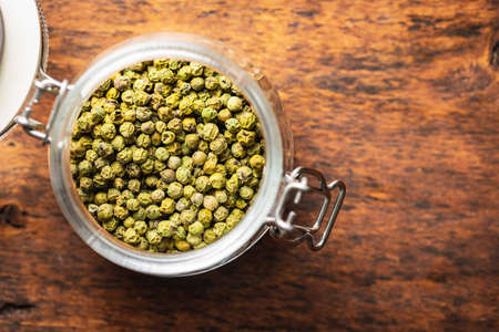 Dried green peppercorn. Dry green pepper spice in jar on wooden table. Top view.の写真素材