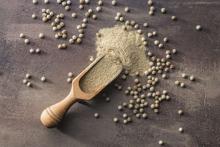 White ground pepper and whole peppercorn spice in a wooden scoop. Top view.