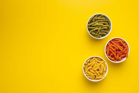 Three colors fusilli pasta. Colorful italian raw pasta in bowl on yellow background. Top view.