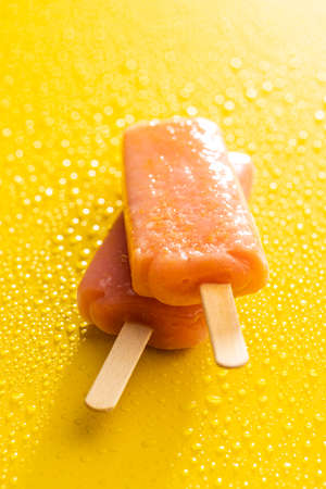 Fruity ice lolly. Sweet ice cream on yellow table with a water drops.