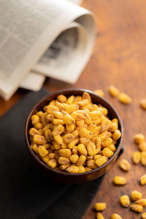 Roasted salted corn snack in bowl on a wooden table.